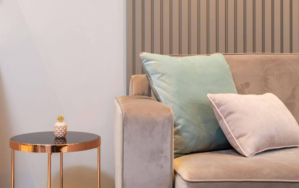 Šviesus, minimalistinis svetainės kampas su švelniai pilka sofa. Šviesios spalvos ir minimalus dekoras padeda mažam kambariui atrodyti erdvesniam.