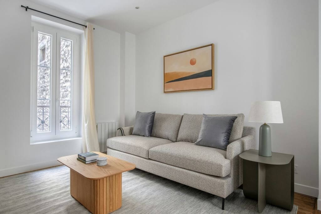 Minimalistinė svetainė su šviesiai pilka sofa, mediniu kavos staliuku, švelnių tonų paveikslu ant sienos ir natūralia dienos šviesa – jaukus ir modernus interjeras, atskleidžiantis, kaip sukurti minimalistinę svajonių svetainę.