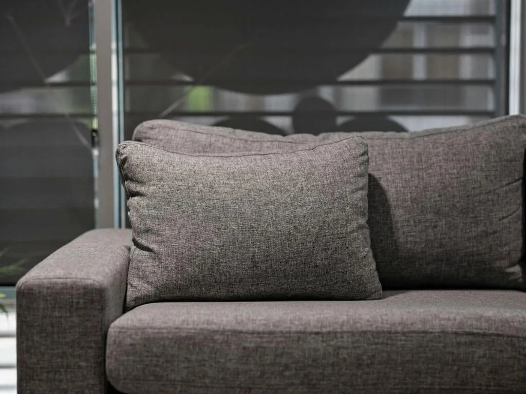 Moderni pilka tekstūrinio audinio sofa su minkšta pagalvėle svetainės fone